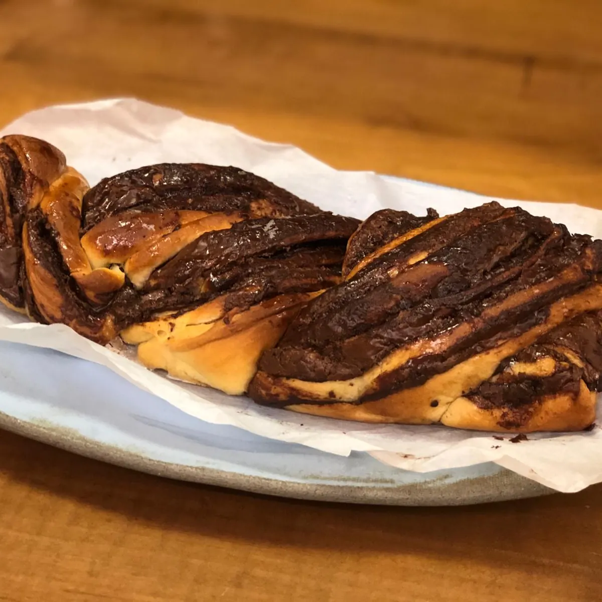 A chocolate babka, twisted and glossy, on a plate lined with baking paper